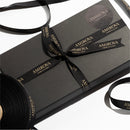 A black gift voucher package with the brand name 'Amirova Cosmetic Clinic' displayed prominently. The package is tied with a black ribbon that has the brand name printed on it.