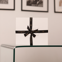 A luxury lip care gift set by Monika Heiligmann packaged in a white box with a black ribbon, displayed on a table.