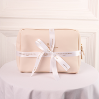 A beige cosmetic pouch with a white ribbon and gold zipper, branded with 'Monika Heiligmann Paris' for lipcare collection.